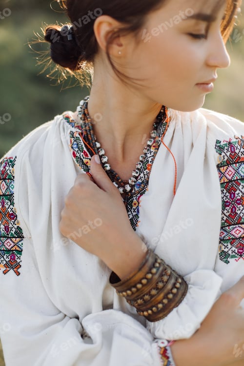 Preview: Young woman in traditional national embroidered shirt and skirt on nature at sunset.