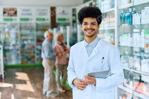 Preview: Happy Muslim pharmacist working in a pharmacy and looking at camera.