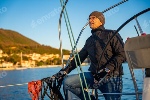 Preview: Young man captain standing at the helm and controls a sailboat during a journey by sea in winter
