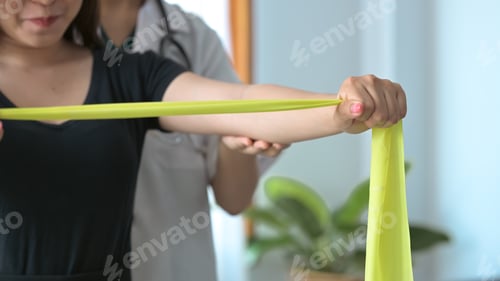 Preview: Physiotherapist assisting female patient do muscle rehabilitation exercising with elastic band.