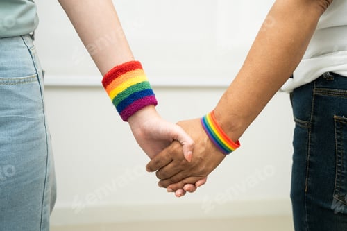 Preview: Asian LGBT couple woman holding hand wearing rainbow wristband.