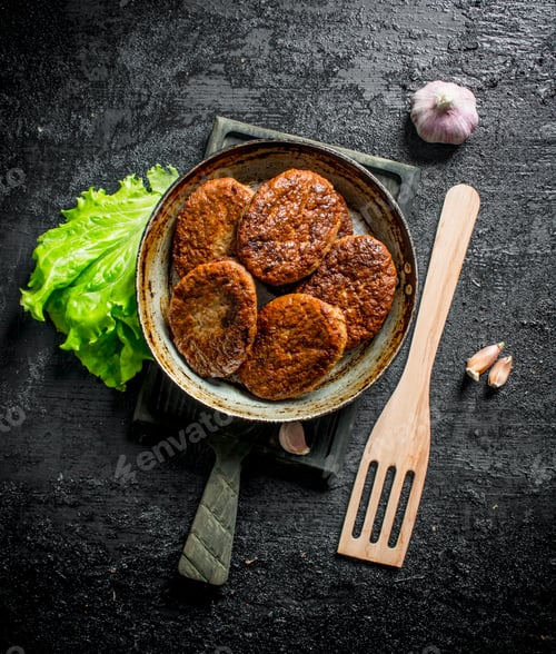 Preview: Cutlets in pan with garlic,salad leaves and a wooden shovel.