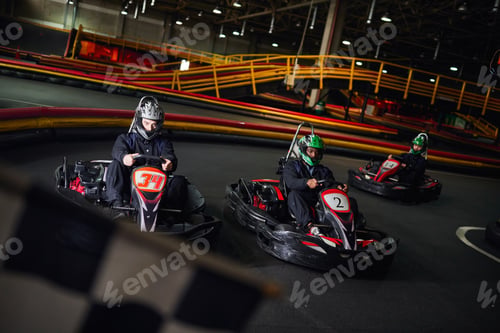 Preview: interracial men driving go kart near checkered black and white racing flag on blurred foreground