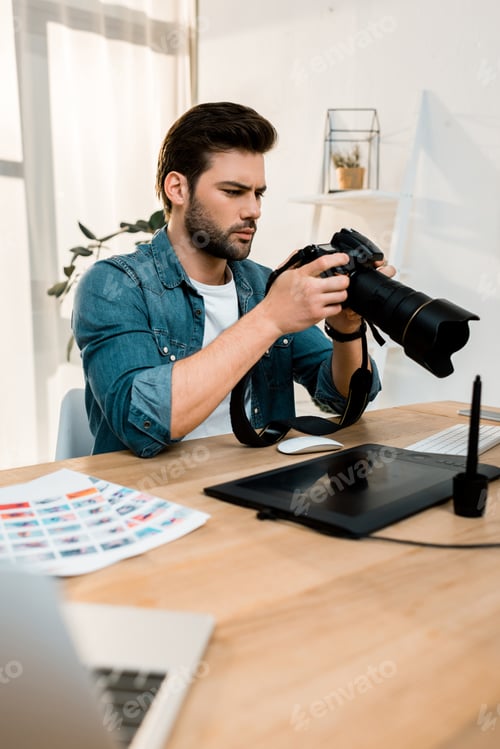 Preview: handsome young photographer using camera at workplace