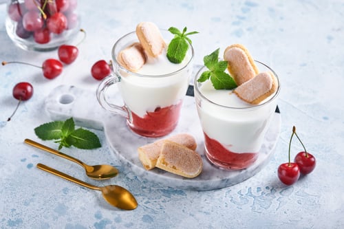 Preview: Summer cherry puff pastry with savoiardi cookies and cream cheese in glass on light grey background.