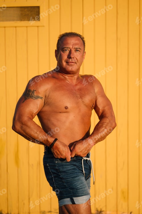 Preview: Muscular older man poses in yellow cabin background.