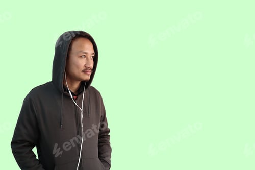 Preview: Man wearing a hoody jacket and using earphones isolated on a light-green background