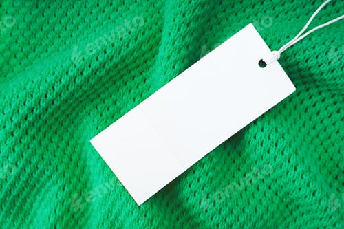 Preview: White blank rectangular clothing tag on green knitted fabric background. Shopping, discount mockup
