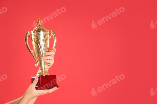 Preview: Child holding golden winning cup on red background, closeup. Space for text
