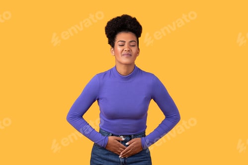 Preview: Unhealthy Hispanic woman touches belly isolated on yellow
