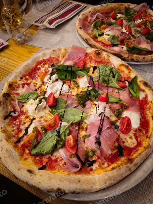 Preview: Delicious pizzas with prosciutto, burrata, pesto and cherry tomatoes resting on restaurant table