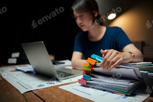 Preview: Young woman working late managing many business documents
