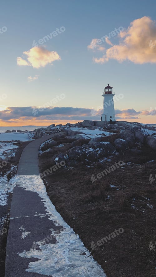 Preview: Vertical shot of a frozen path leading to Peggy's Cove lighthouse at sunset in Canada