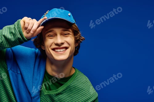 Preview: Young man showcases modern fashion with a cheerful smile against a vibrant blue backdrop