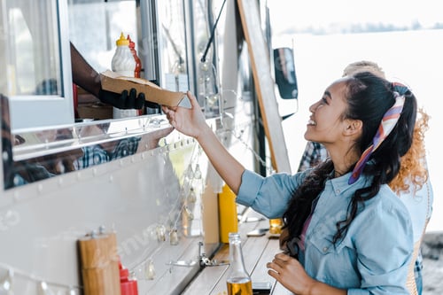 Preview: cropped view of african american man giving carton plate to asian girl near food truck