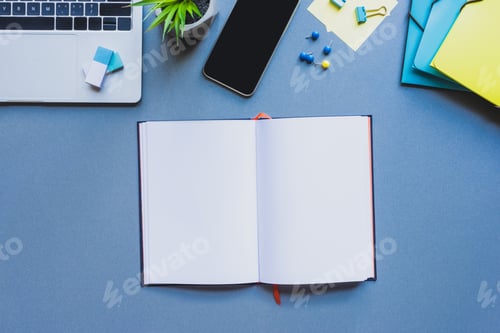 Preview: Top view of open notebook near digital devices and office supplies on blue surface