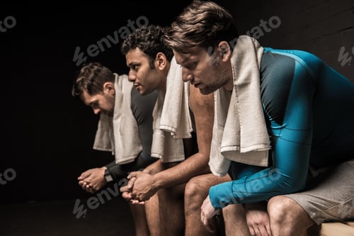 Preview: Tired male athletes resting at gym locker room