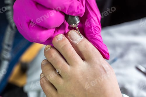 Preview: Pedicurist master in pink gloves cuts the cuticle and shellac toe nails in the pedicure salon