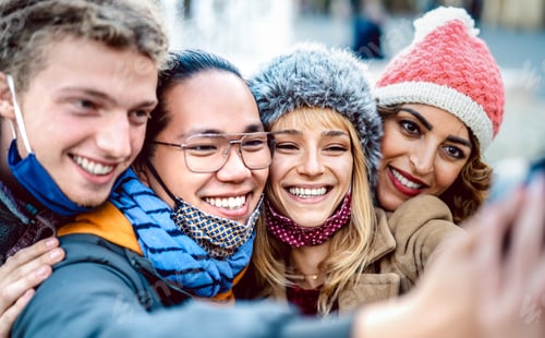 Preview: Multicultural travelers taking happy selfie wearing face mask and winter clothes