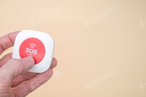 Preview: Elderly hand holding a wireless SOS emergency alarm button isolated on light brown background