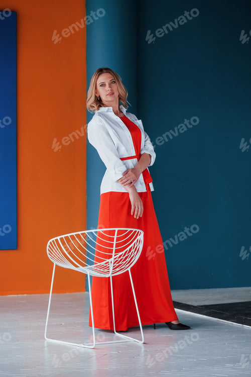 Preview: Beautiful blonde in festive red dress is in the room with orange and blue colored walls