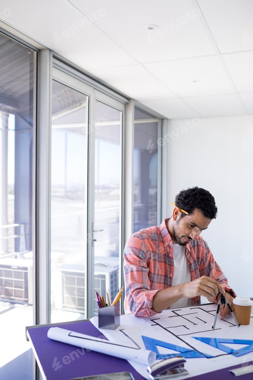 Preview: Male architect working on blueprint over drafting table