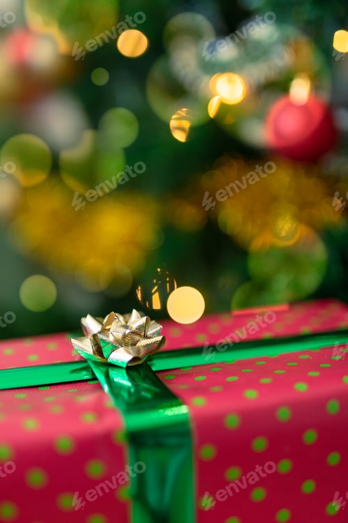 Preview: Christmas present in red paper with gold ribbon standing over christmas tree