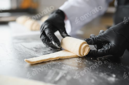 Preview: Baker rolling dough for croissants in bakery kitchen