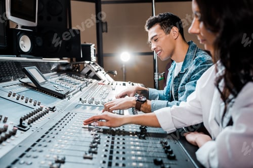 Preview: two young multicultural sound producers working at mixing console i recording studio