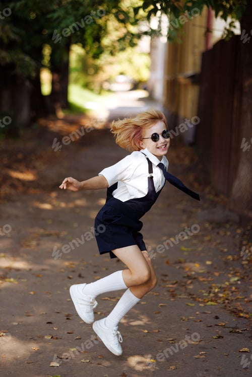 Visualização: Menina em uniforme escolar pulando no ar com as mãos para cima. De volta à escola.