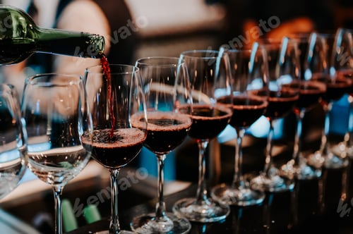 Preview: Bartender pours red wine in glasses at bar.Male sommelier pouring red wine into long-stemmed