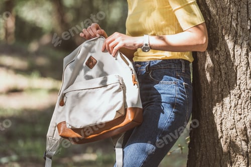 Preview: partial view of woman with backpack leaning on tree in park