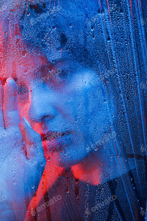 Preview: Rainy day. Studio shot in dark studio with neon light. Portrait of beautiful girl behind wet glass