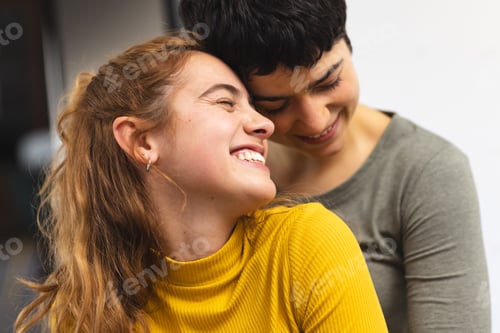 Preview: Happy biracial lesbian couple embracing and smiling at home