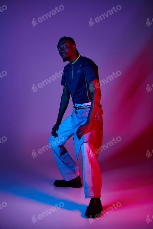 Preview: Stylish young African American man posing with neon lights in a vibrant studio setting