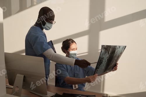 Preview: African American assistant pointing at x-ray image held by female radiologist