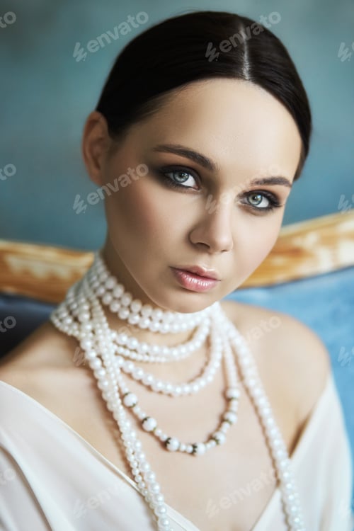Preview: Beautiful slender brunette girl sitting on the sofa in a long white dress. Portrait of a woman