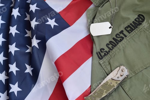 Preview: Military dog tag token and knife lies on Old US Coast Guard uniform and folded United States Flag