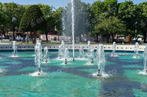Preview: Fountain in city park with green trees at sunny day
