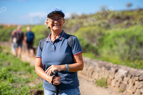 Preview: Happy senior woman walking in a sunny day on trail outdoors on country excursion.