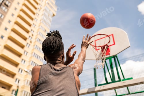 Vista previa: Vista trasera del joven jugador de baloncesto africano lanzando una pelota en la canasta