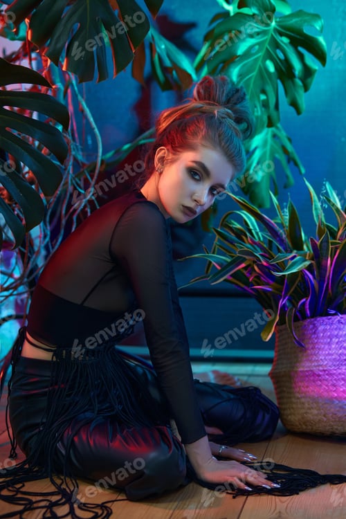 Preview: Young woman surrounded by vibrant tropical plants, wearing black leather outfit and long-sleeved