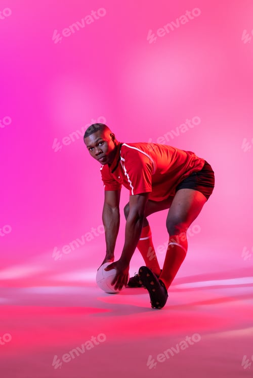 Preview: African american male rugby player catching rugby ball over pink lighting