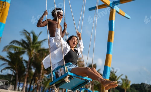 Preview: Happy interracial couple enjoying a fun beach day, swinging under palm trees on a tropical vacation