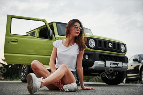 Preview: Sits and resting near new vehicle. Pretty woman in the green modern car posing for the camera