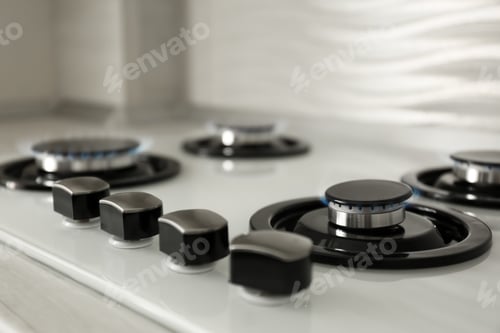 Preview: Gas burners with blue flame on modern stove, closeup