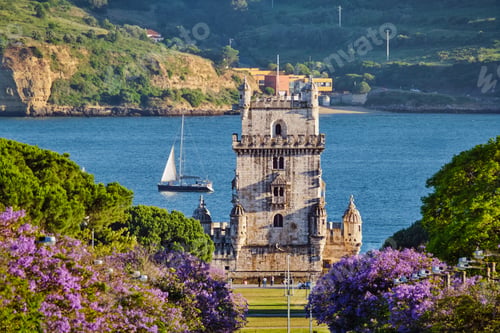 Preview: Scenic Belem Tower in Lisbon framed by blooming jacaranda trees during sunset