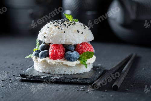 Preview: Aromatic sushi burger with sesame and berries on dark plate.