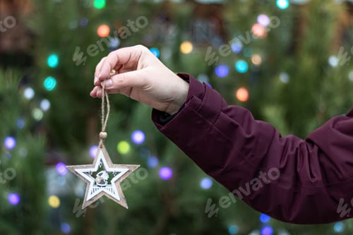 Preview: Christmas tree toy-wooden star, held by a woman's hand on the background of a bokeh