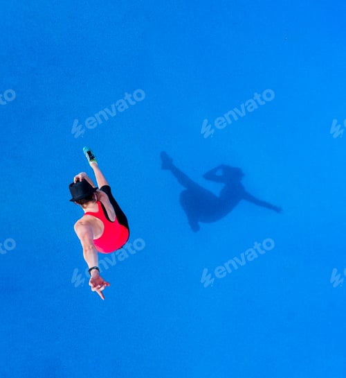 Preview: Jumping young woman and her shadow on blue background, top view